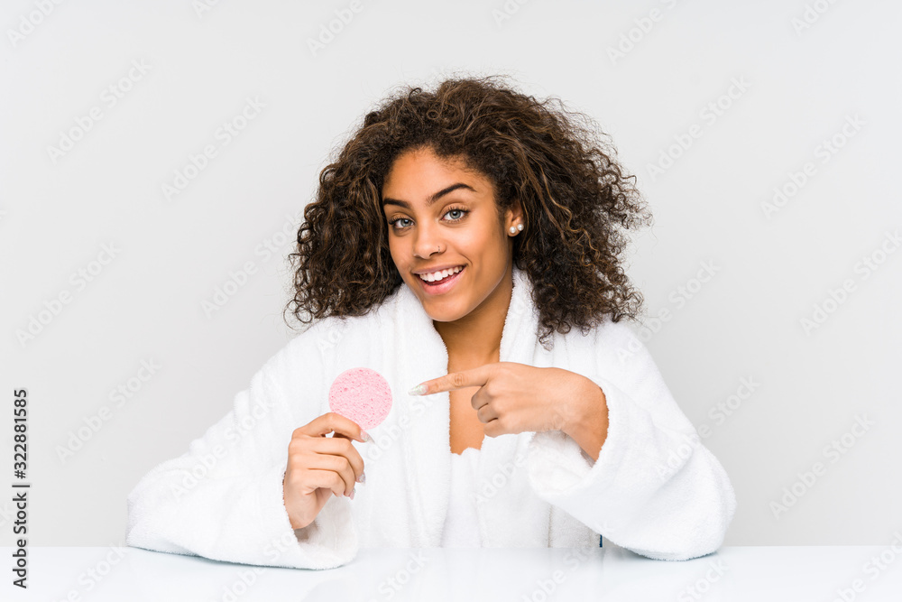 Young african american woman using a facial disk smiling cheerfully pointing with forefinger away. Young african american woman using a facial disk smiling cheerfully pointing with forefinger away.
