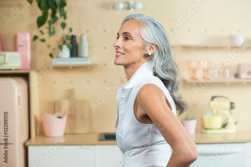 Standing in a  modern kitchen, A youthful middle-aged woman with gray hair looks off camera., Studio City, CA, USA photo