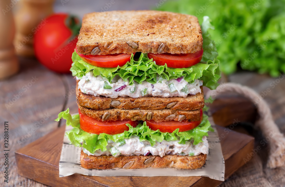Stack of tuna salad sandwich on multigrain bread with tomato, lettuce and mayonnaise on wooden board. Rustic wooden background. Selective focus. Stack of tuna salad sandwich on multigrain bread with tomato, lettuce and mayonnaise on wooden board. Rustic wooden background. Selective focus.