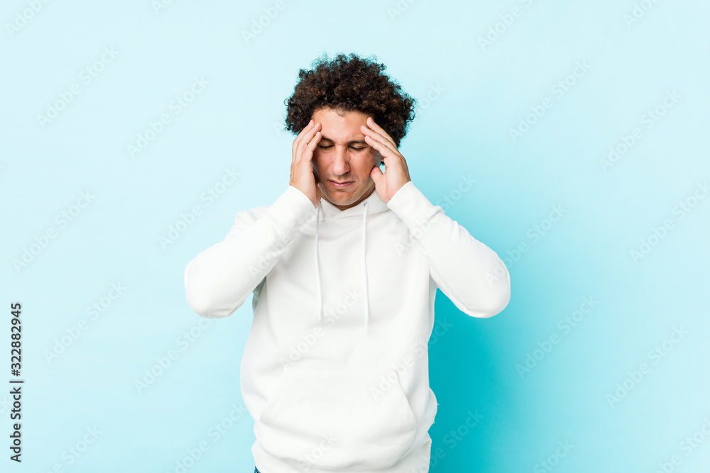 Young sporty man against a blue background touching temples and having headache. Young sporty man against a blue background touching temples and having headache.