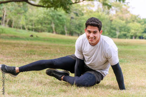 Handsome young man practicing yoga on green grass in the public park. Athletic male wear sportswear while doing yoga at outdoors. Healthy lifestyle concept.