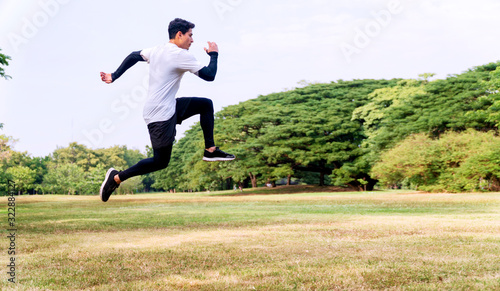 Handsome young man athlete runner with energy exercise training and jumping outdoors with big green tree in the public park. Active healthy and motivation lifestyle and ambition Concept