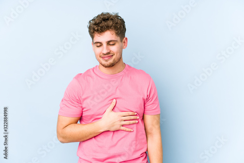 Young blond curly hair caucasian man isolated touches tummy, smiles gently, eating and satisfaction concept.