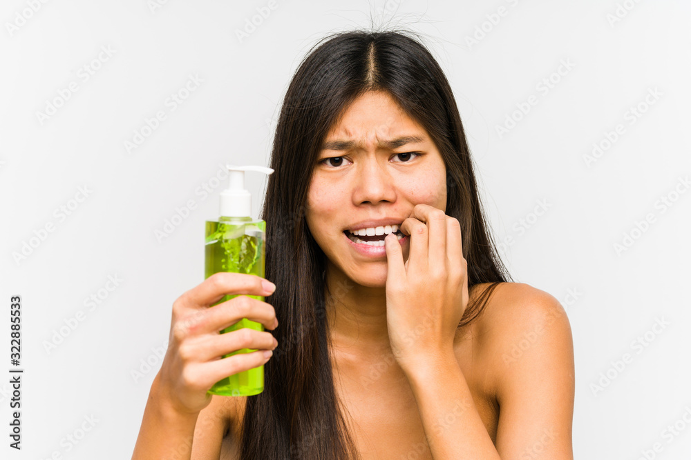 Young chinese woman holding a moisturizer with aloe vera isolated biting fingernails, nervous and very anxious. Young chinese woman holding a moisturizer with aloe vera isolated biting fingernails, nervous and very anxious.