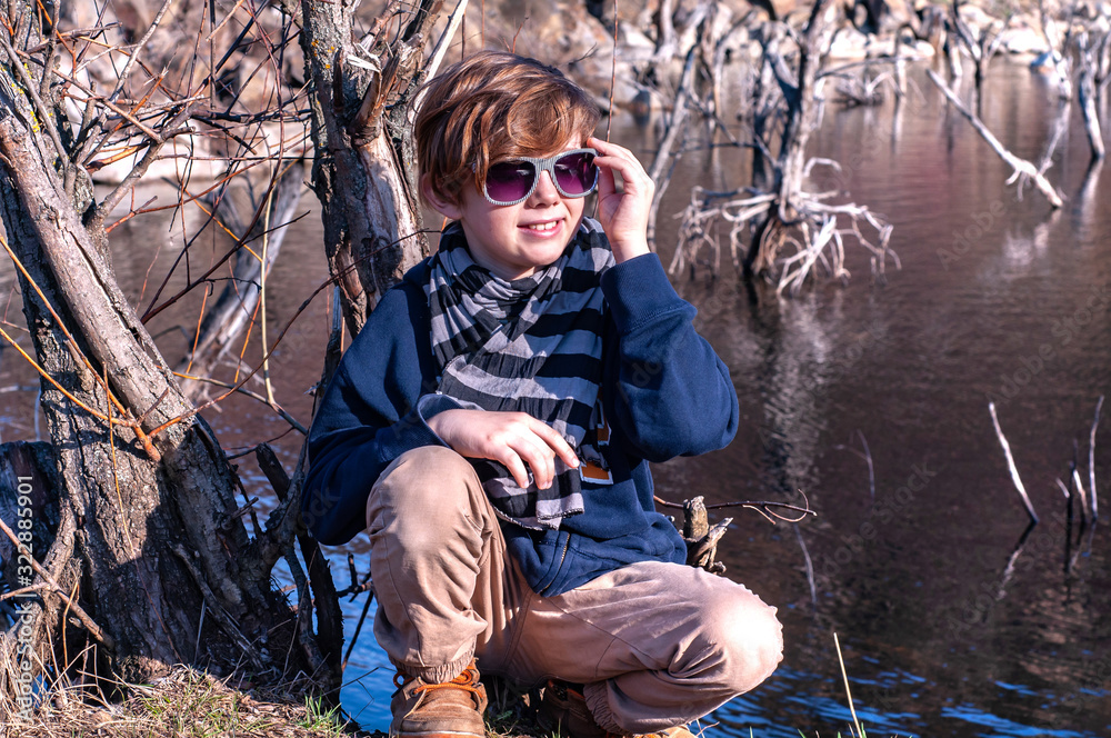 Fashionable boy model posing on the background of the lake in sunglasses outdoors. Spring autumn clothes