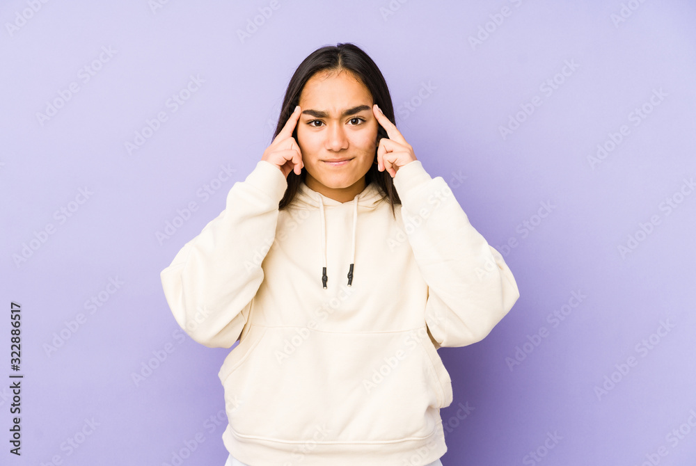 Young woman isolated on a purple background focused on a task, keeping forefingers pointing head. Young woman isolated on a purple background focused on a task, keeping forefingers pointing head.