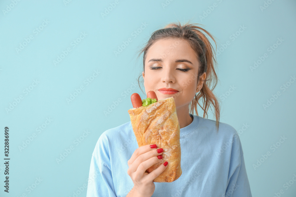 Portrait of beautiful young woman with French hot dog on color background