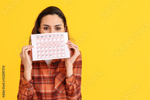 Young woman with menstrual calendar on color background