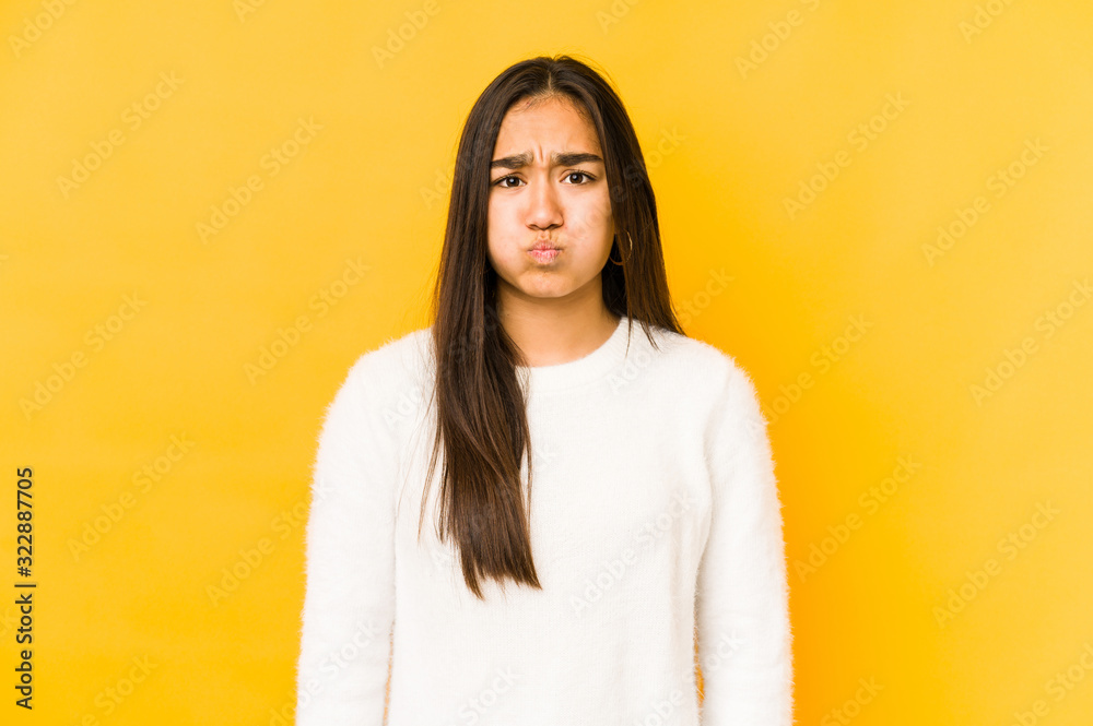Young woman isolated on a yellow background blows cheeks, has tired expression. Facial expression concept. Young woman isolated on a yellow background blows cheeks, has tired expression. Facial expression concept.