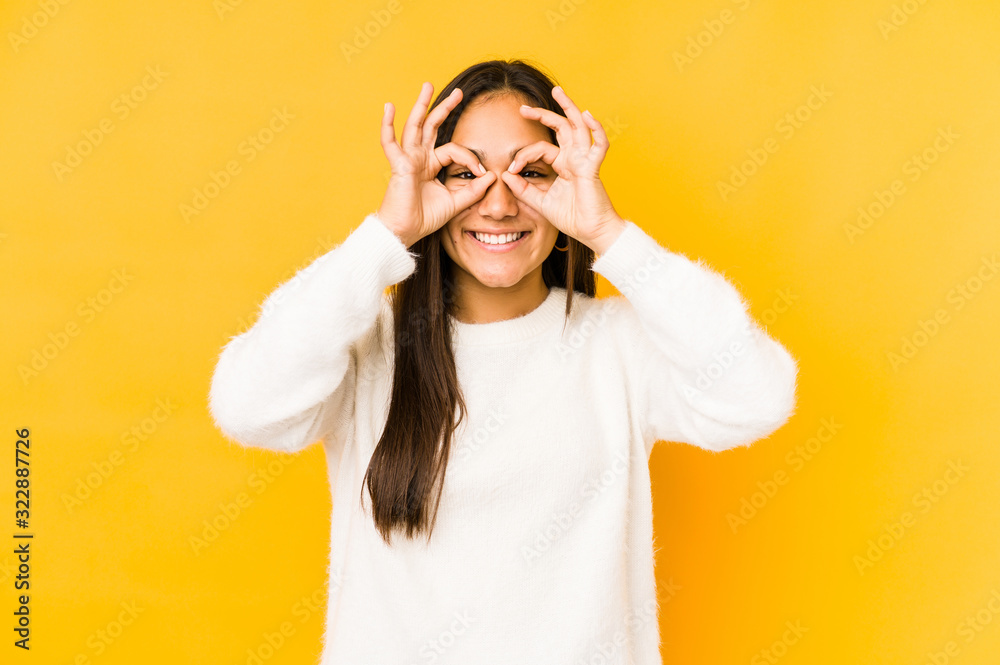 Young woman isolated on a yellow background showing okay sign over eyes Young woman isolated on a yellow background showing okay sign over eyes