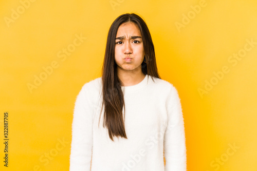 Young woman isolated on a yellow background blows cheeks, has tired expression. Facial expression concept.