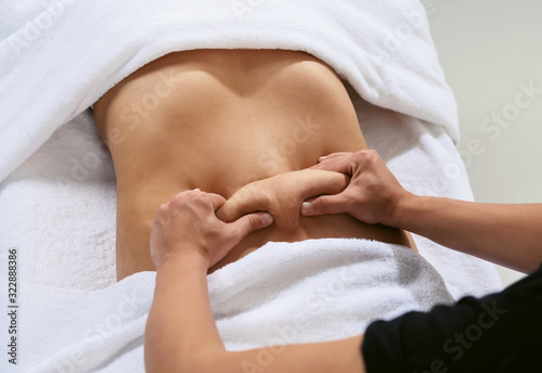 Masseur pulls hand the skin on the abdomen, showing the body fat in the abdominal area and sides. Treatment and disposal of excess weight, the deposition of subcutaneous fat.