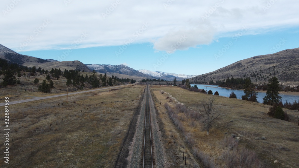 Rail road track as a leading line through a grass valley surrounded by tree covered rolling hills and a snow covered mountain range Rail road track as a leading line through a grass valley surrounded by tree covered rolling hills and a snow covered mountain range