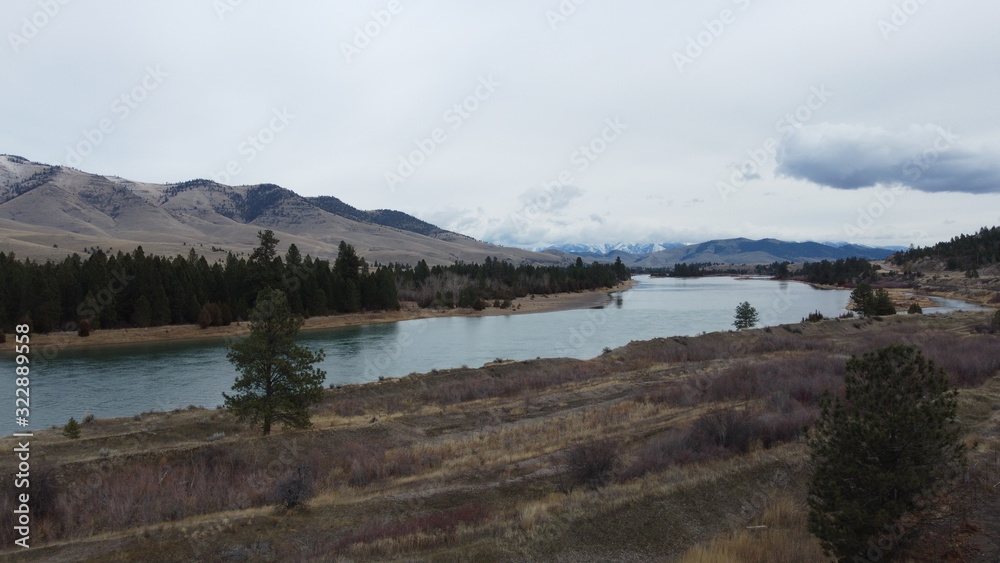 Large river winding through a valley with rolling grass hills and snow covered mountains in the distance