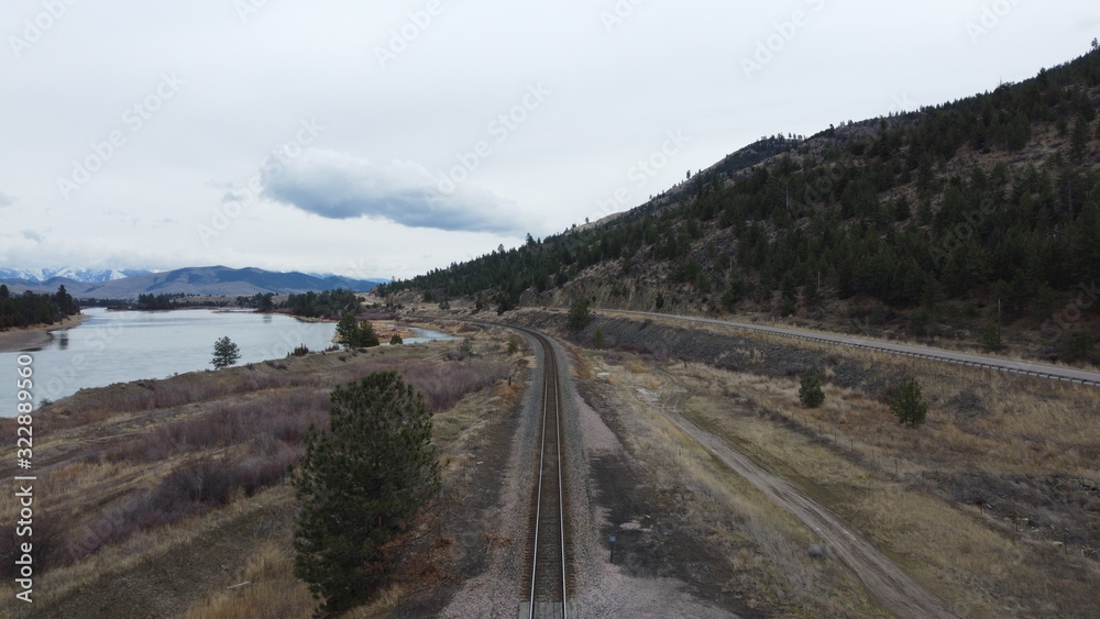 Train track and road bending around curve of mountain range with river on the side Train track and road bending around curve of mountain range with river on the side