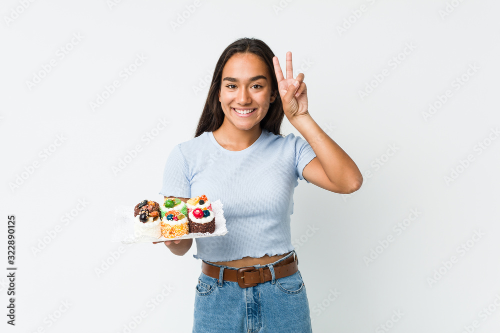 Young mixed race indian holding a sweet cakes showing victory sign and smiling broadly. Young mixed race indian holding a sweet cakes showing victory sign and smiling broadly.