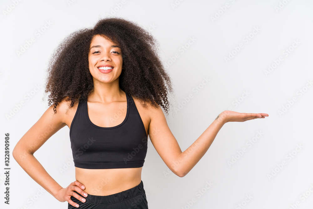 Young african american sporty woman showing a copy space on a palm and holding another hand on waist. Young african american sporty woman showing a copy space on a palm and holding another hand on waist.