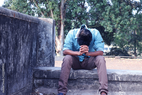 Depressed Teenager man sitting alone on Wall in Outdoor.Unpleasant pain. Sad unhappy handsome man.Bangladeshi and Asia boy Suffering Depression.