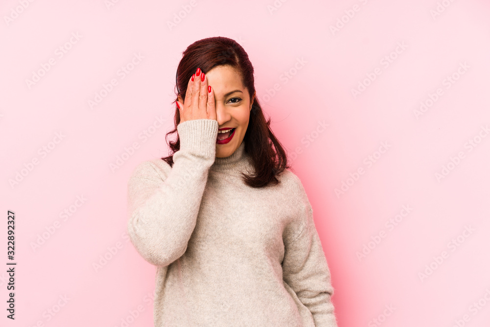 Middle age latin woman isolated on a pink background having fun covering half of face with palm. Middle age latin woman isolated on a pink background having fun covering half of face with palm.