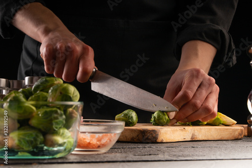 Cooking salad or sauce by a cook. Cutting brussels sprouts. On a black background, horizontal photo. Advertising, cooking, recipe book, home meals, restaurant business.