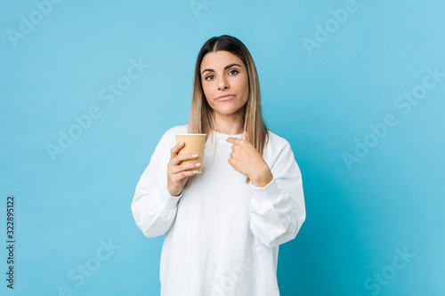 Young caucasian woman holding a takeaway coffee pointing with finger at you as if inviting come closer.