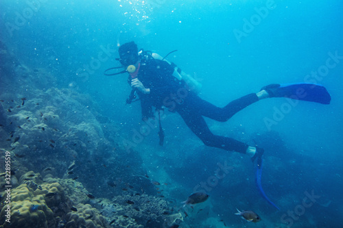 Scuba diver diving on tropical reef with blue background and reef fish at Gulf of Thailand