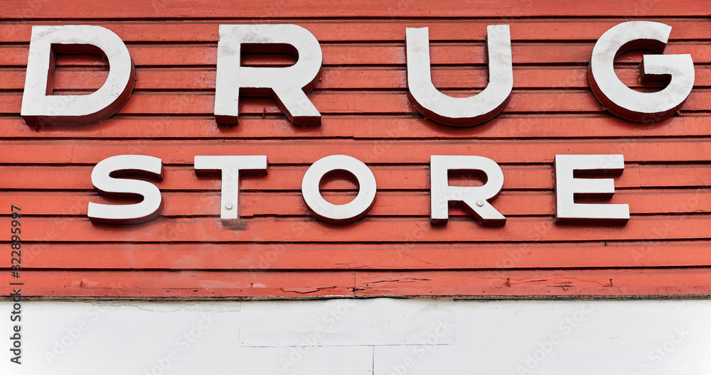 Obraz premium Close-up of a drug store sign over the entrance of a pharmacy in Asia. White painted letters are fixed on red peeling off painted wooden panels