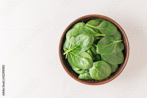 A clay bowl with spinach leaves on a white wooden table. Food for fitness. The view from the top.