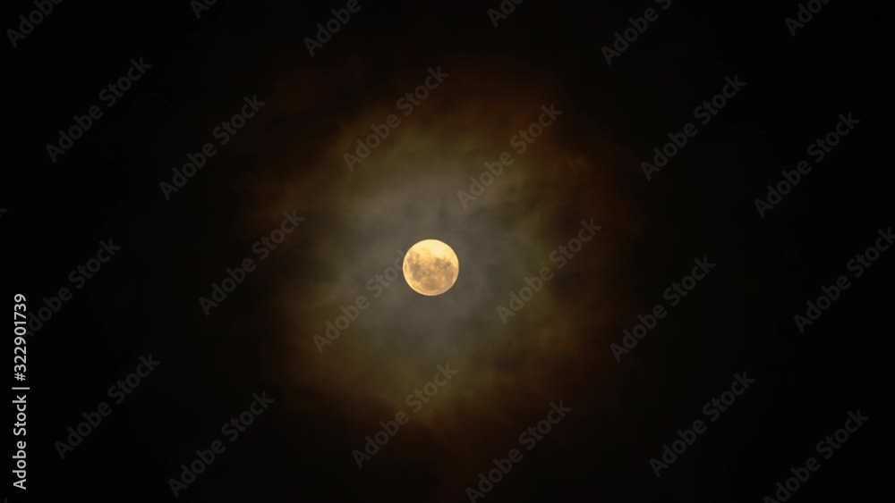 Full glowing yellow moon with clouds being blown by winds during storm at nights.