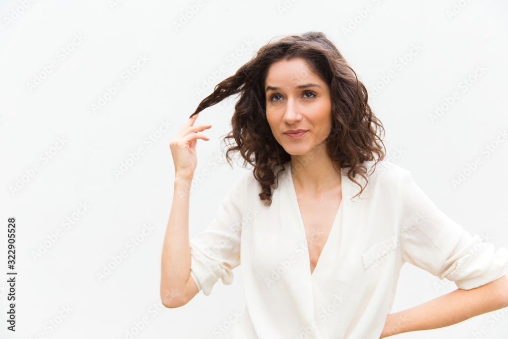 Attractive young lady holding strand of hair. Daydreaming curly woman thinking about something. Dreaming, fantasizing concept Attractive young lady holding strand of hair. Daydreaming curly woman thinking about something. Dreaming, fantasizing concept