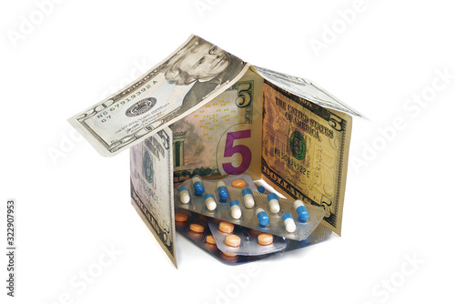 heap of pills in blister packs inside a house made from dollar banknotes isolated on white background