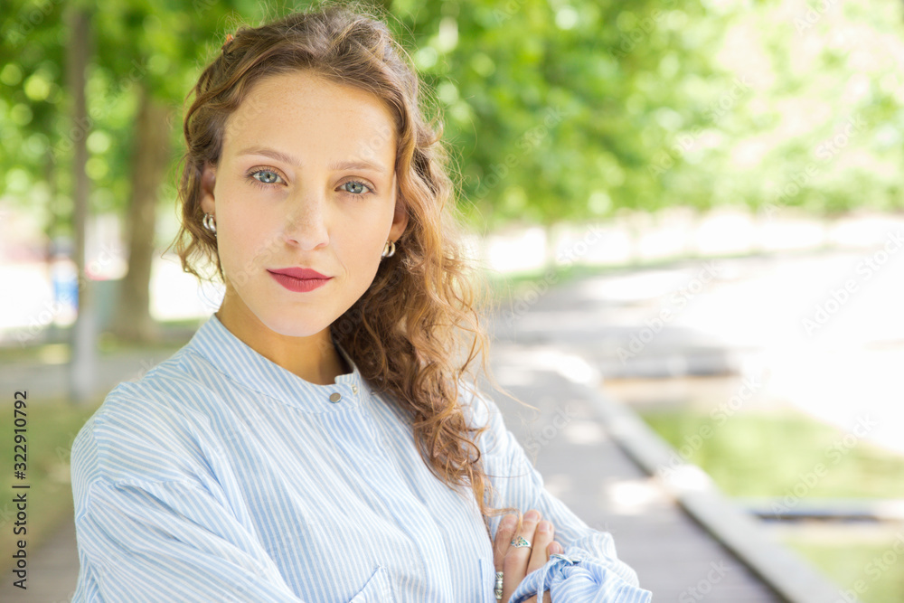 Closeup shot of confident curly young woman looking at camera. Cheerful lady with crossed arms posing in spring park. Confidence concept Closeup shot of confident curly young woman looking at camera. Cheerful lady with crossed arms posing in spring park. Confidence concept