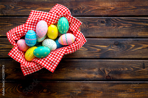 Basket with painted eggs for Easter dinner on dark wooden desk top-down copy space