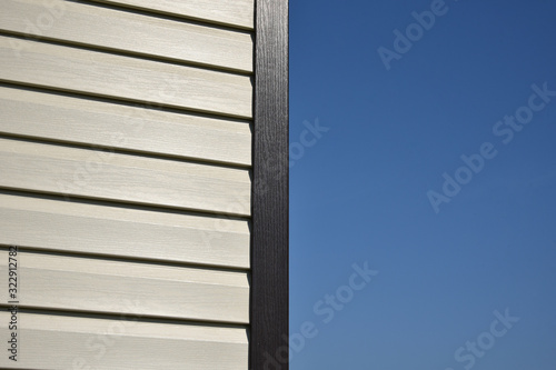 White vinyl siding wall surface with horizontal lines. texture of siding panels. Background for construction companies. Corner of a new residential private house. Blue sky background.