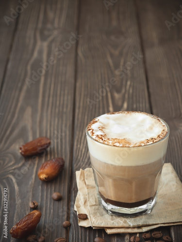 Glass cup of coffee with milk on a dark wooden background. Hot latte or cappuccino prepared with milk on a rustic wooden table with copy space. Near dates fruits.