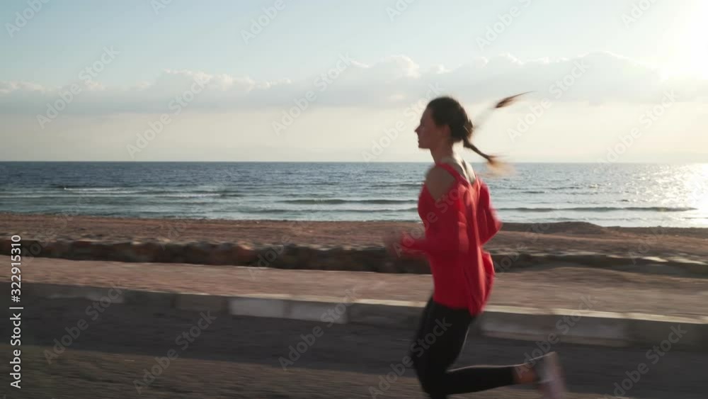 Beautiful young girl running on promenade at sunset near ocean
