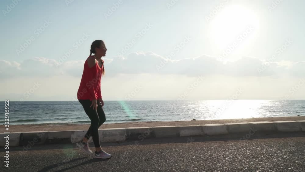 Sportive young woman jogging on seaside and stops to catch her breath