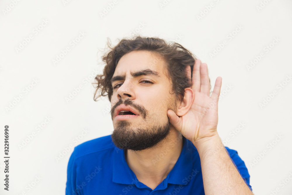 Confused young man holding hand near ear. Stylish guy gesturing cannot hear or talk louder. Say what, repeat, cannot hear concept Confused young man holding hand near ear. Stylish guy gesturing cannot hear or talk louder. Say what, repeat, cannot hear concept