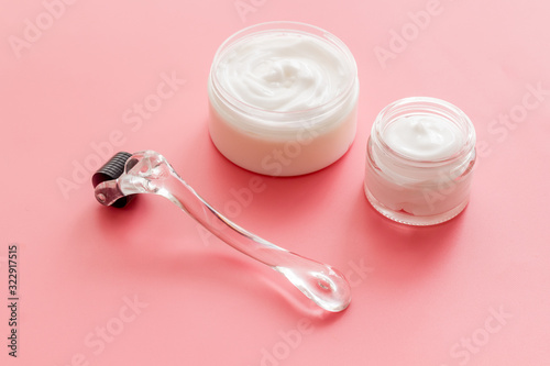 Dermaroller for home cosmetologic procedure near creams on pink background
