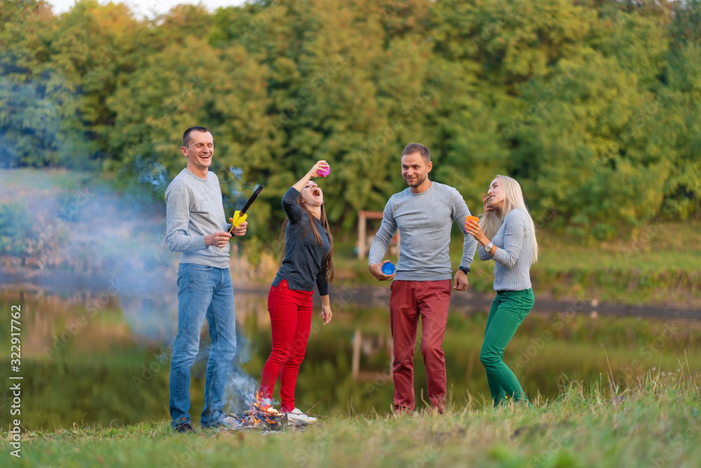Obraz premium Picnic with friends in at lake near bonfire. Company friends having hike picnic nature background. Hikers relaxing during drink time. Summer picnic. Fun time with friends
