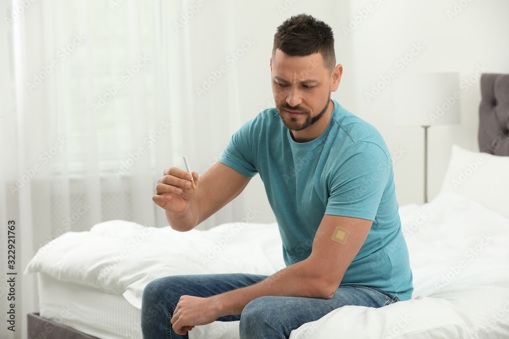 Emotional man with nicotine patch and cigarette in bedroom