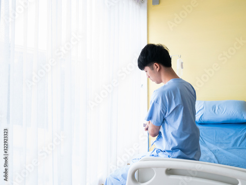 Asian patient young male alone and lonely sitting with stress for waiting professional doctor or practitioner nurse to take care of recovery physical body for stand again without tripod cane in clinic