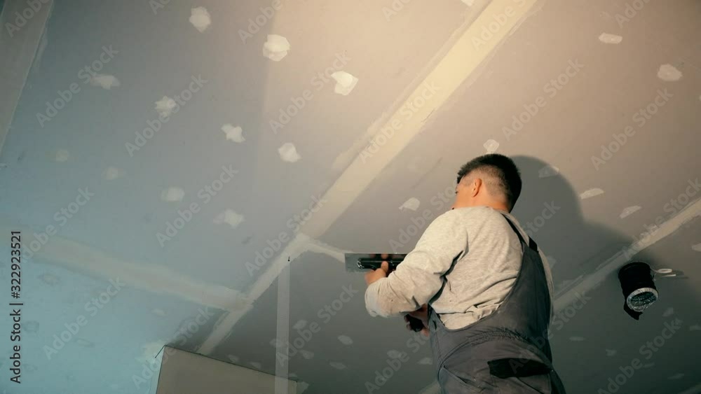 Professional worker smoothing gypsum plasterboard frame with spackling paste