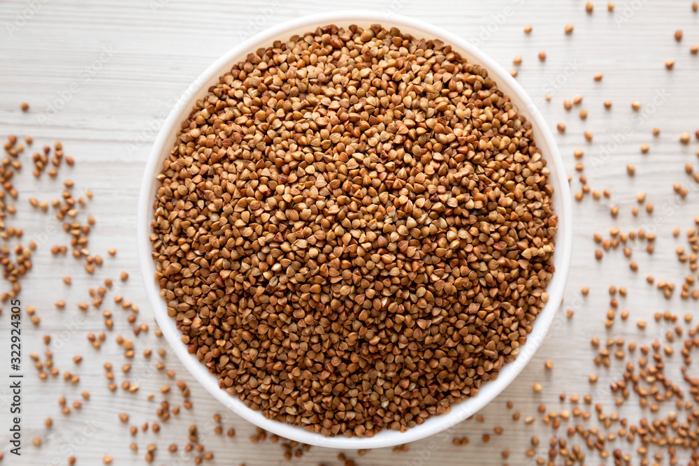 Uncooked Roasted Buckwheat in a white bowl on a white wooden background, top view. Flat lay, overhead, from above. Close-up. Uncooked Roasted Buckwheat in a white bowl on a white wooden background, top view. Flat lay, overhead, from above. Close-up.