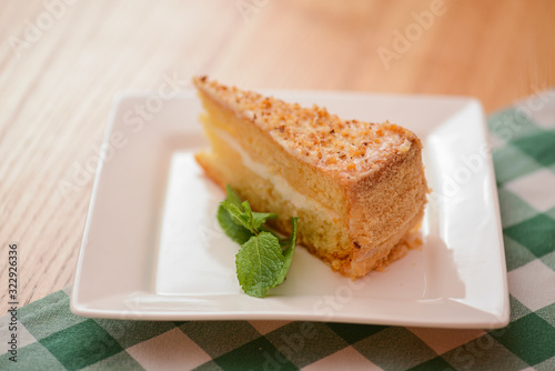 Slice of victoria sponge cake with cream filling, served with a mint leaf on a white plate on light wooden table