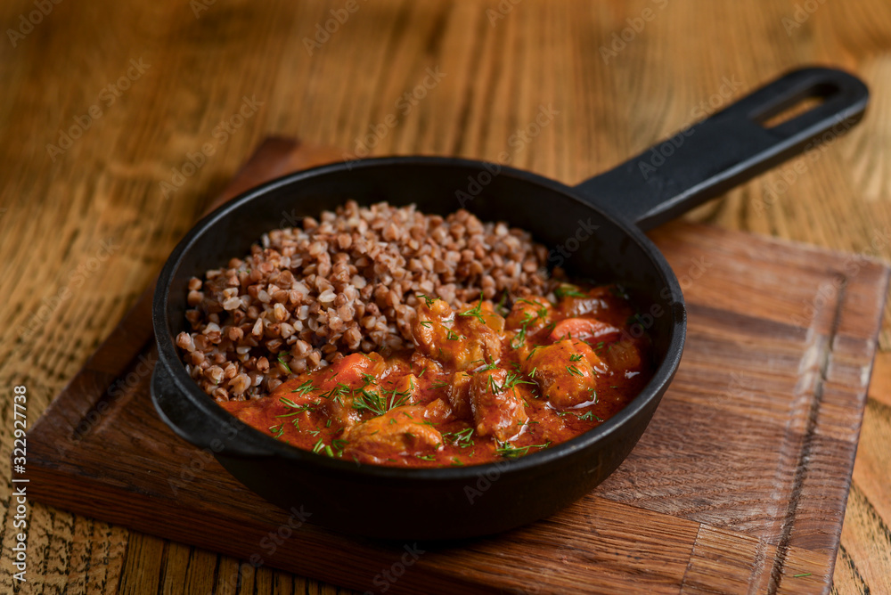 Healthy food. Boiled buckwheat with meat gravy and vegetables served in a pan over dark wooden table background. Healthy food. Boiled buckwheat with meat gravy and vegetables served in a pan over dark wooden table background.