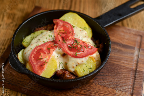 Meat and mushroom gratin with cheese and tomatoes served in a pan over dark wooden table background. Ukrainian cuisine.