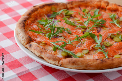 Delicious Italian pizza with salmon fish served on white plate on rustic wooden table with plaid tablecloth.