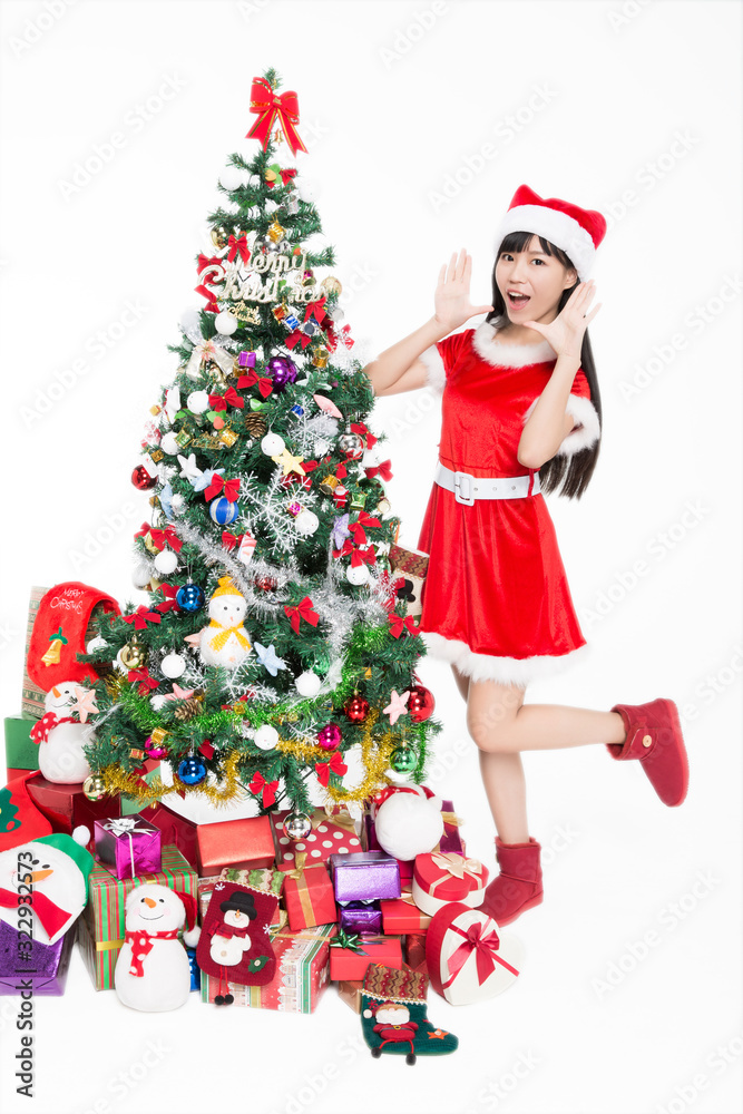 Pretty girl wearing santa costumes standing by christmas tree on white background. Pretty girl wearing santa costumes standing by christmas tree on white background.