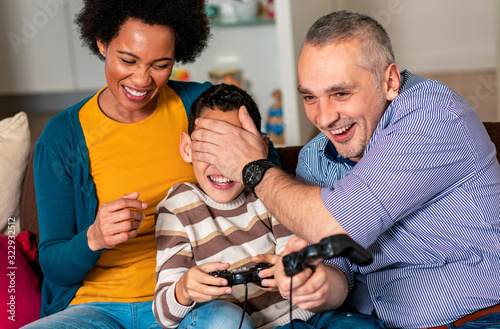 Smiling mixed race family enjoying time at home sitting on sofa in living room and playing video games. © Zoran Zeremski